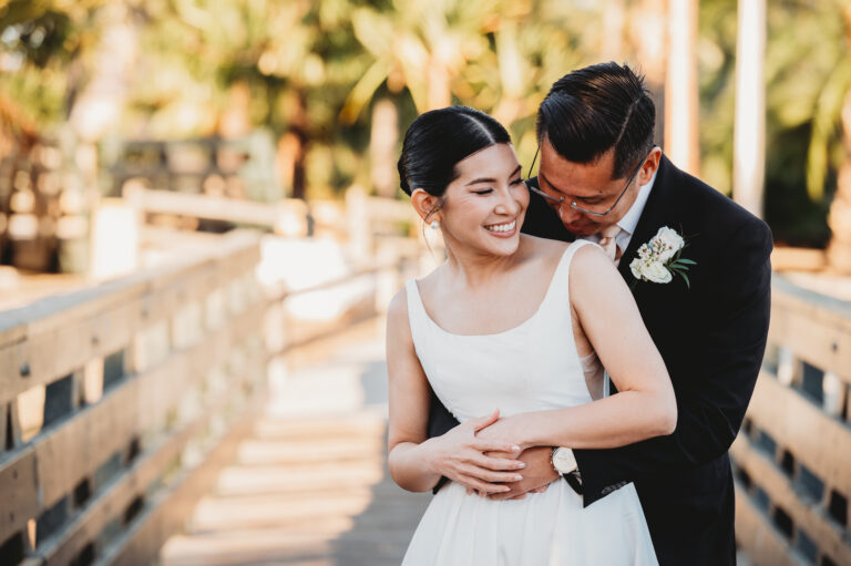 Happy couple embracing on their wedding day while walking across a bridge.