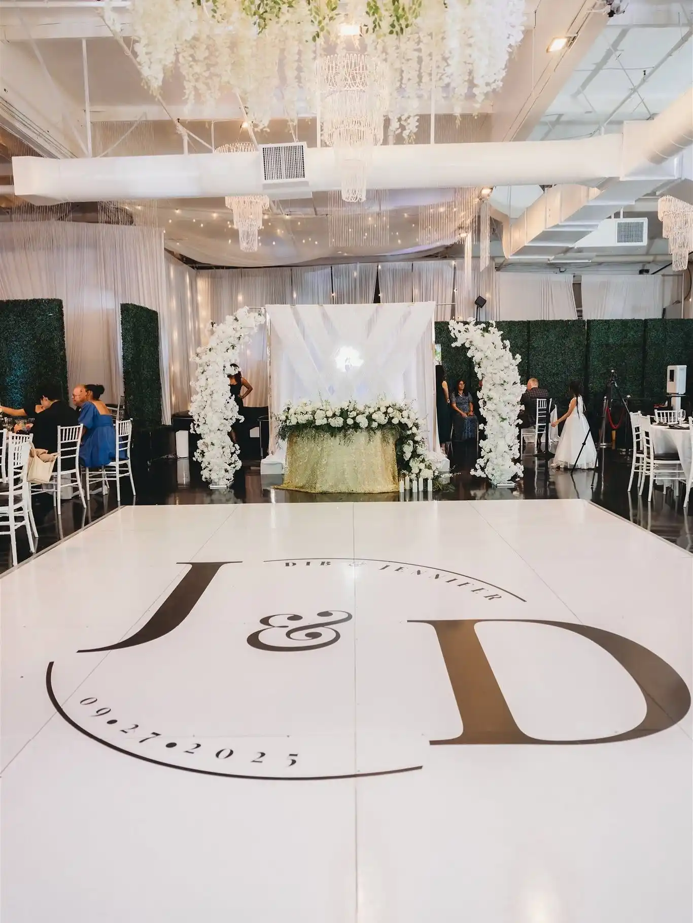 White dance floor with a custom couple’s monogram leading to a sweetheart table framed by white floral arches, hedge walls and crystal chandeliers at Serendipity The Venue in Fountain Valley, CA